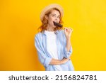 Young woman eat ice creams with chocolate glaze on yellow background. Funny redhead girl with summer straw hat lick ice cream.