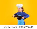 Small photo of Kid chef cook with cooking pot stockpot. Kid chef cook prepares food on isolated studio background. Kids cooking. Teen boy with apron and chef hat preparing a healthy meal.