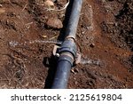 Small photo of Water dripping from a leaky pipe in farm land. Water flows from a rusty pipe. Constant stream of water coming from a pipe. or Water bursts out of a leaking plumbing pipe laid on the ground