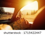 Woman's legs in sneakers in the window car with road map. Summer travel. Modern hipster girl resting in a car and reading a map. Woman with feet on car door. Feet outside the window at sunset. 