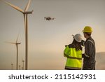 Two engineers working and holding the report at wind turbine farm Power Generator Station on mountain,Thailand people,Technician man and woman discuss about work,Use drone view from high angle