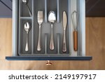 Kitchen drawer with cutlery set. Flat lay view of organizer tray with simple kit of utensils in open storage box. Clean and silver spoons, forks, knives and whisk for cooking lying together