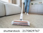 Housework and housekeeping concept. Selective focus at brush on modern and cordless vacuum cleaner. Cropped woman using professional appliance to hoovering carpet at home