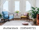 Small photo of Two comfortable armchairs stand opposite each other, next to a coffee table with tulips in vase. Interior design in the style of the 60s. Old fashioned furniture in living room. Hygge apartment