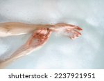 Skincare, bodycare and everyday beauty routine concepts. Top view of woman hands over hot water in bubble bath. Female holding arms together, making gentle touch to soft skin
