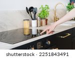 cropped shot of female hand press sensor button and using electrical hob for cooking dinner at home kitchen with stylish interior, modern household appliances concept