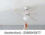 cropped shot of female hand pull switch of ceiling fan with lamp on white background with copy space, room cooling and ventilation concept
