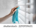 Small photo of Close up view of woman cleaning white window blinds with a blue microfibra rag indoors. Housework and housekeeper concepts