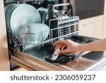 Small photo of Close up view of female hand inserting dishwasher tablet into open built-in dishwasher machine with utensils inside in modern home kitchen. Household, housekeeping, domestic concept