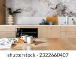 dish towel, fresh croissant and ceramic cups of tea on bamboo tray on wooden tabletop with sun light on kitchen background interior, breakfast concept