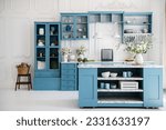 Kitchen in scandinavian style with island table, blue furniture and modern kitchenware. Bright interior with white walls and floor. Vase with flowers on marble countertop.