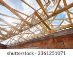 Roof trusses on new residential housing development construction site. Red brick family home with wooden attic against blue sky with sunlight. Concept of rooftop renovation and repairing process