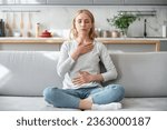 Small photo of Concept of mental health. Woman sitting on couch and doing calming breathing exercises after panic attack. Female inhaling and exhaling to deep breath. Self-control, anxiety relief concept
