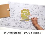 Town planning and land use planning - hand holding a measuring ruler in front of a zoning of plots, on a cadastral plan placed on a desk