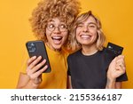 Small photo of Easy payments. Happy young women make internet shopping use mobile phone and banking card purchase things online smile broadly dressed in casual t shirt isolated over vivid yellow background