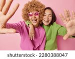 Small photo of Positive overjoyed women keep arms outstreched laugh happily dressed in green and pink jumpers embrace and foolish around smile gladfully poses indoor. Friendship positive emotions and fun concept