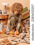Small photo of Professional female jointer repairs old wooden furniture uses marker pen poses in workshop with various tools concentrated with her handicraft wood working job. Woman carpenter produces chair