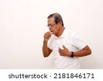 Small photo of Side view of asian old man standing while coughing and holding his chest. Isolated on white