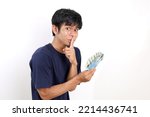 Young asian man standing while holding Indonesian banknotes with silent gesture or kept secret concept