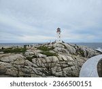 Small photo of Peggy's Cove, NS, CAN, August 15, 2023 - The Peggy's Cove lighthouse with some tourists standing on the rocks around it on a cloudy summer day.