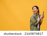 Small photo of Young Asia lady using phone with positive expression, smiles broadly, dressed in casual clothing feeling happiness and stand isolated on yellow background. Happy adorable glad woman rejoices success.