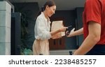 Small photo of Young happy Asian woman accept paper bag from delivery man with bicycle in red uniform carry case box scan QR code payment on smartphone in front of house. express food delivery concept.