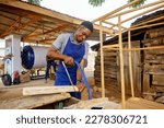 african carpenter holding a tape wearing apron working cutting sawing