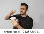 Small photo of Young man looks at the credit cards on his hand and gets very upset and angry. Overspent money and owed. Stressed due to high expenses. Isolated gray background.