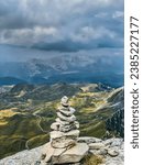 Small photo of Pyramid of stones built high in Durmitor mountains, Montenegro. Cairns or rock piles on mountain top overlooking highlands with green valley and curvy road. Stone cairn tower on summit of Prutas.