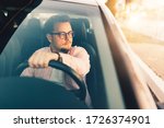 A young european happy driver in comfortable expensive car. Stylish man wearing glasses. View through the windshield