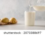 Small photo of Pouring vegan potato milk in glass and potato in bowl on light background. Close up. Plant based milk replacer and lactose free. Dairy free