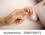 Small photo of The newborn baby in a white closes has a firm grip on the parent's finger after birth. Close-up little hand of child and palm of mother and father. Parenting, childcare and healthcare concept.