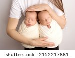 Small photo of Tiny newborn twins boys in white cocoons in their mother's arms. The mother holds the twin children in her arms. Studio professional photography of newborn twins.