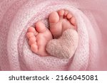 Knitted pink heart in the legs of a baby. Soft feet of a new born in a pink wool blanket. Close-up of toes, heels and feet of a newborn. Macro photography the tiny foot of a newborn baby. 