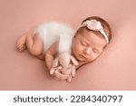 Top view of a newborn baby girl sleeping in a white jumpsuit with pink rabbit a white bandage and a pink flower on her head on a pink background. Beautiful portrait of a little girl 7 days, one week.