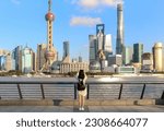 Female tourist on the Shanghai Bund taking a picture of the iconic Shanghai skyline view of Lujiazui. Shanghai a massive international city in China.