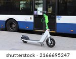 White and green electric kick scooter standing on the road with blue and white bus moving on the background. Scooter sharing in Tel Aviv, Israel
