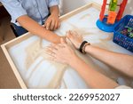 Fragment. Therapeutic activities with children. A doctor helps a patient with autism play with sand.