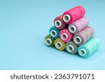 Set of different colorful sewing threads on light blue background, flat lay. With space for text.