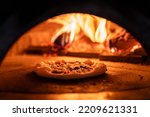 Small photo of Pizza concept. Preparing traditional italian pizza. Long shovel for pizza, baking dough in a professional oven with open fire in interior of modern restaurant kitchen