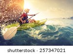 Young lady paddling hard the kayak with lots of splashes near the cliff at sunny day