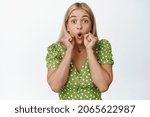 Small photo of Surprised blond girl pucker lips, say wow and looking amazed, hear shocking announcement, standing in green dress over white background