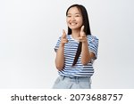 Small photo of You got this. Cheerful asian girl congratulating you, pointing fingers at camera and smiling happy, praising, making a compliment, standing over white background