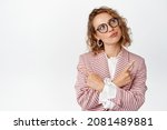 Thoughtful business woman in glasses and stylish suit, looking intrigued and pointing sideways, making decision, thinking, picking from variants, white background