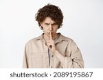 Small photo of Close up of angry curly man shushing, making shut up shush gesture and staring threatening, white background