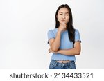 Intrigued asian woman looking thoughtful, thinking of something, having assumption, standing in blue tshirt over white background