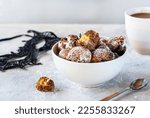 Small photo of Italian traditional Carnival fritters or balls toped with sugar powder in white bowl over concrete background with carnival mask, cacao mug and tea spoon. Carnival celebration concept