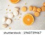 Orange and Vanilla French Macaroons with orange fruit filling on a creamy white clay background, decorated with small chamomiles and fresh sliced oranges