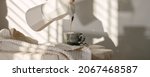 Small photo of Pouring coffee from Italian coffee maker with into grey espresso craft cup on solid wood stump decorated with linen tea towel in creamy tones against white wall on sunlight creating beautiful shadows