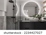 Modern minimalistic bathroom interior design with grey stone tiles, black furniture, eucalyptus in glass vase, round mirror.  Aesthetic simple interior design concept.